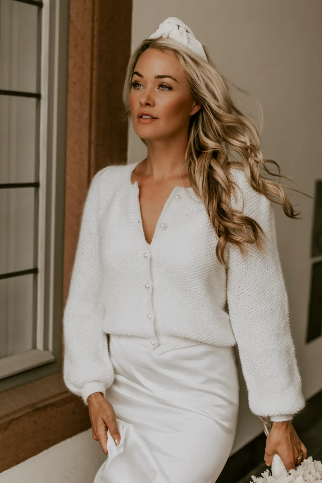 Eine Braut trägt den eleganten Brautcardigan SWEET LOLA in Ivory mit Perlenknöpfen und weiten Ärmeln zu einem schlichten Brautkleid.