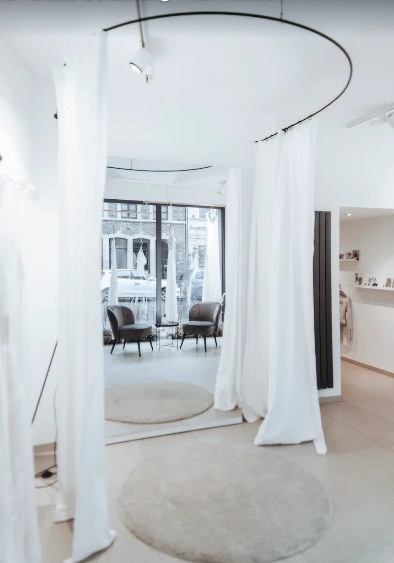 Heller, minimalistischer Showroom mit großen Spiegeln, weißen Vorhängen und gemütlicher Sitzecke vor einem Schaufenster. Die Atmosphäre wirkt ruhig, stilvoll und einladend.